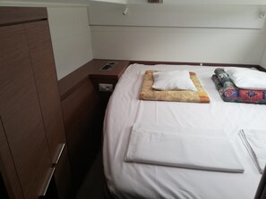 A neatly made bed with a white comforter, a folded blanket, and a colorful throw. There is a wooden nightstand with a lamp and a power outlet.
