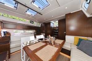 A boat interior with a dining area, white cushioned seating, and a kitchen area with a stove and sink. - Sun-Kissed Sailing Adventure in Split, Croatia (Split)