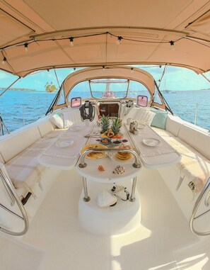 A boat's dining area with a table set for two, surrounded by cushioned seating, and a canopy overhead.
