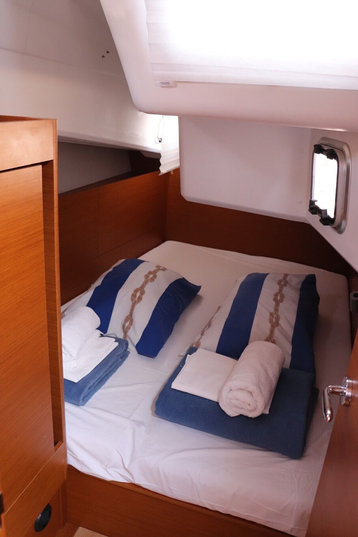 A compact bed with blue and white bedding, a small window, and a wooden door.
