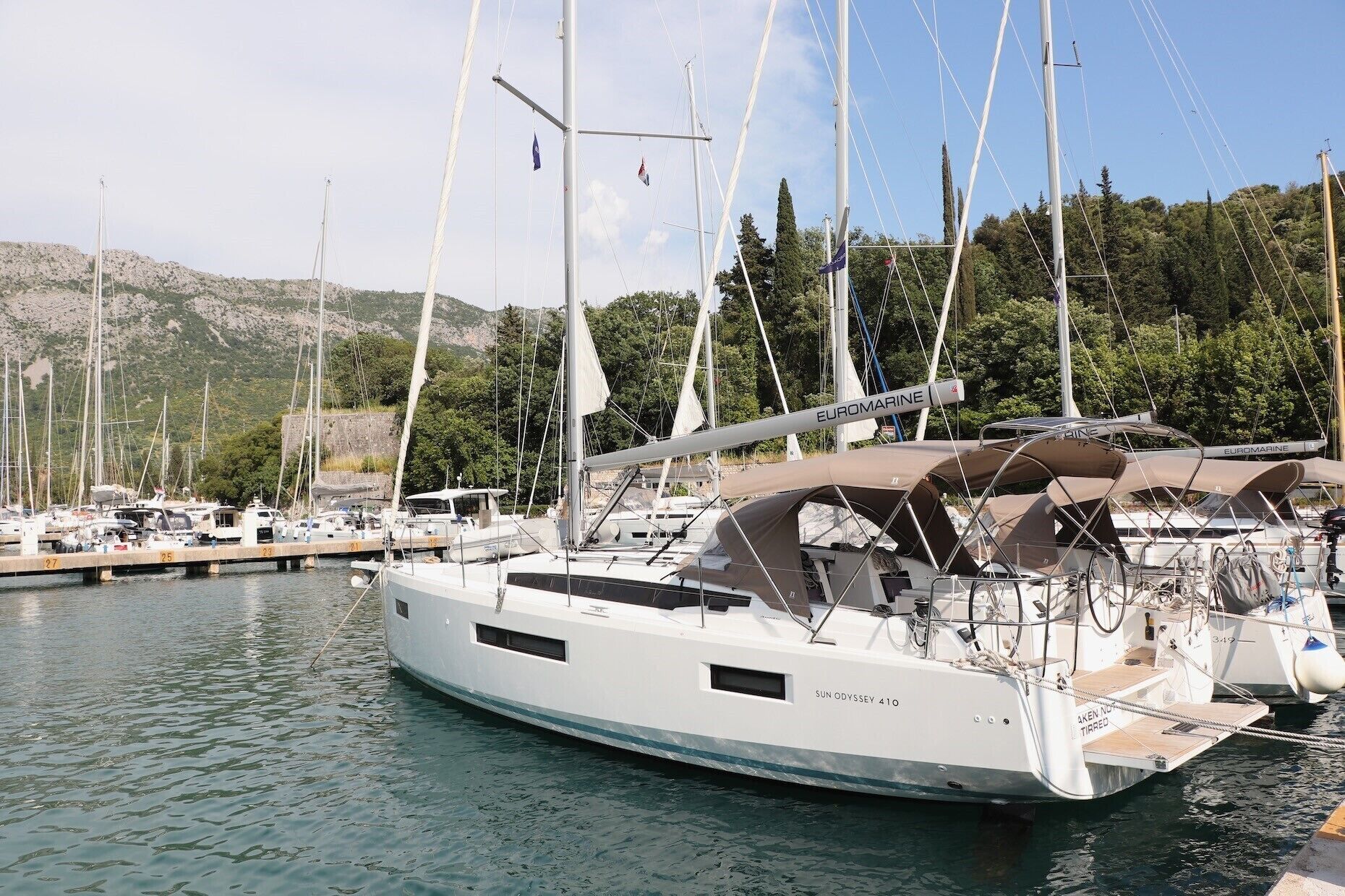 Una marina con diverse barche a vela ormeggiate, tra cui uno yacht bianco chiamato SUN ODYSSEY 41C.
