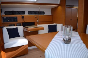 A compact boat interior with a dining table, two cushioned seating areas, a control panel, and a small cabinet. - Dubrovnik Delight: Sun-soaked Sailing Adventure (Ploce)