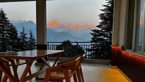 Une table et des chaises en bois, disposées sur un balcon offrant une vue sur la montagne.