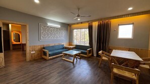 Une pièce avec un plancher en bois, un ventilateur de plafond, un canapé, une table et une fenêtre avec des rideaux.