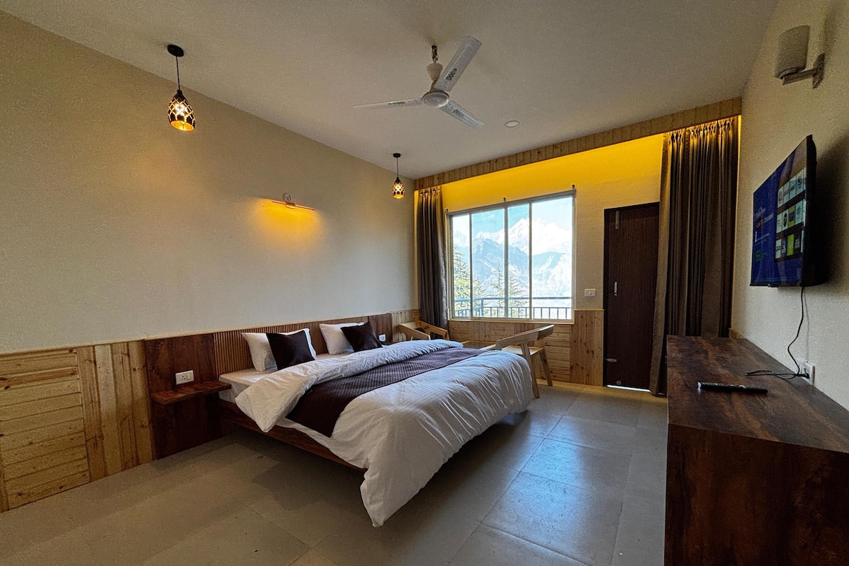 A bedroom with a bed, a desk, a ceiling fan, and a window with a mountain view.