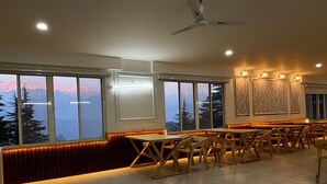 Un espace repas avec des tables et des chaises, de grandes fenêtres offrant une vue sur les montagnes et un ventilateur de plafond.
