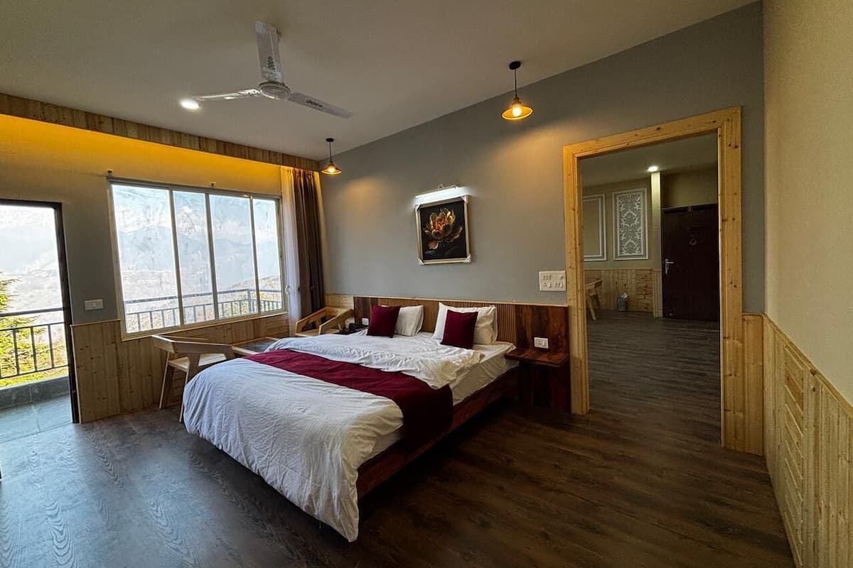 A bedroom with a large bed, a desk, and a view through a window.