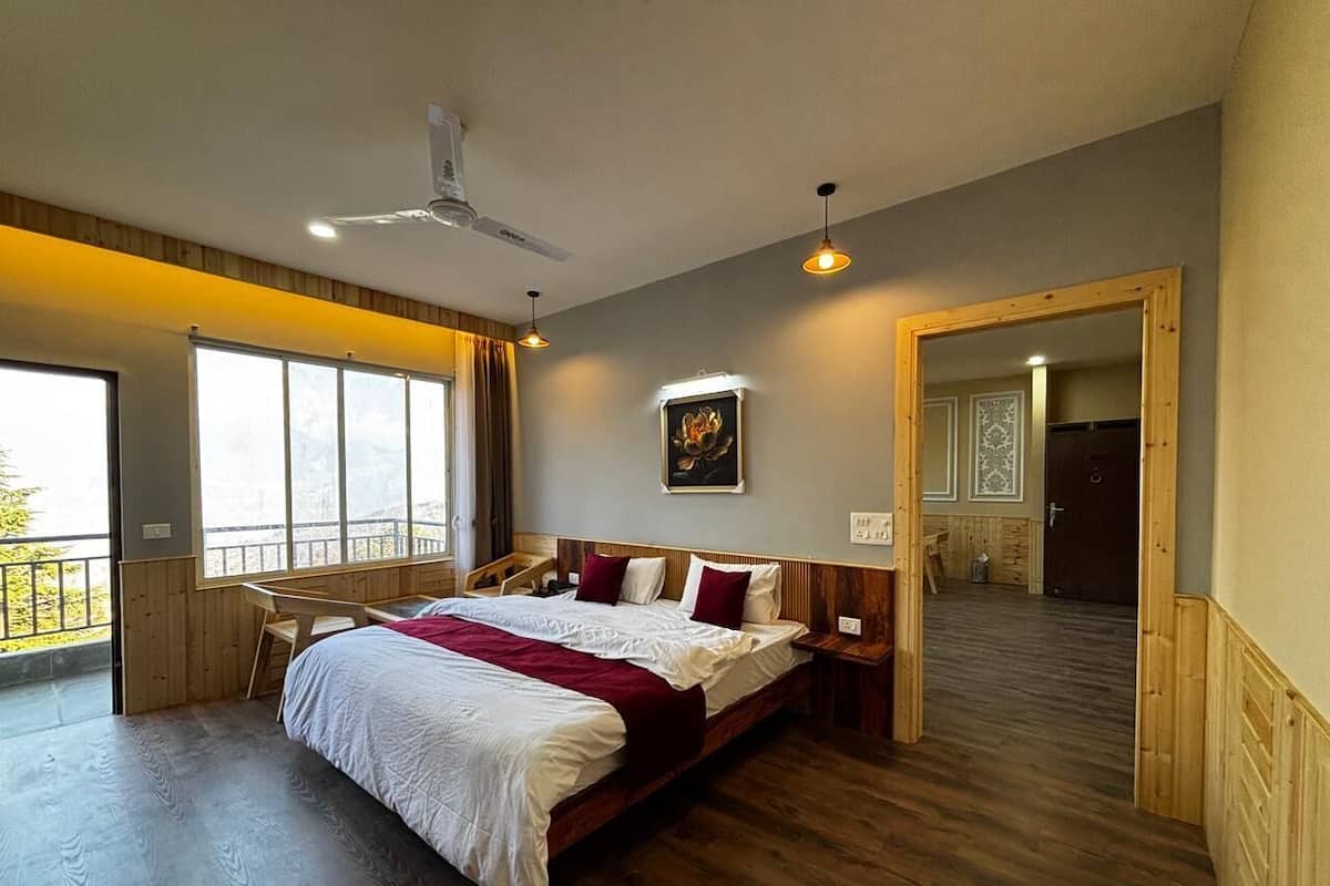 A spacious bedroom with a large bed, a ceiling fan, a wooden desk, and a view through a large window.