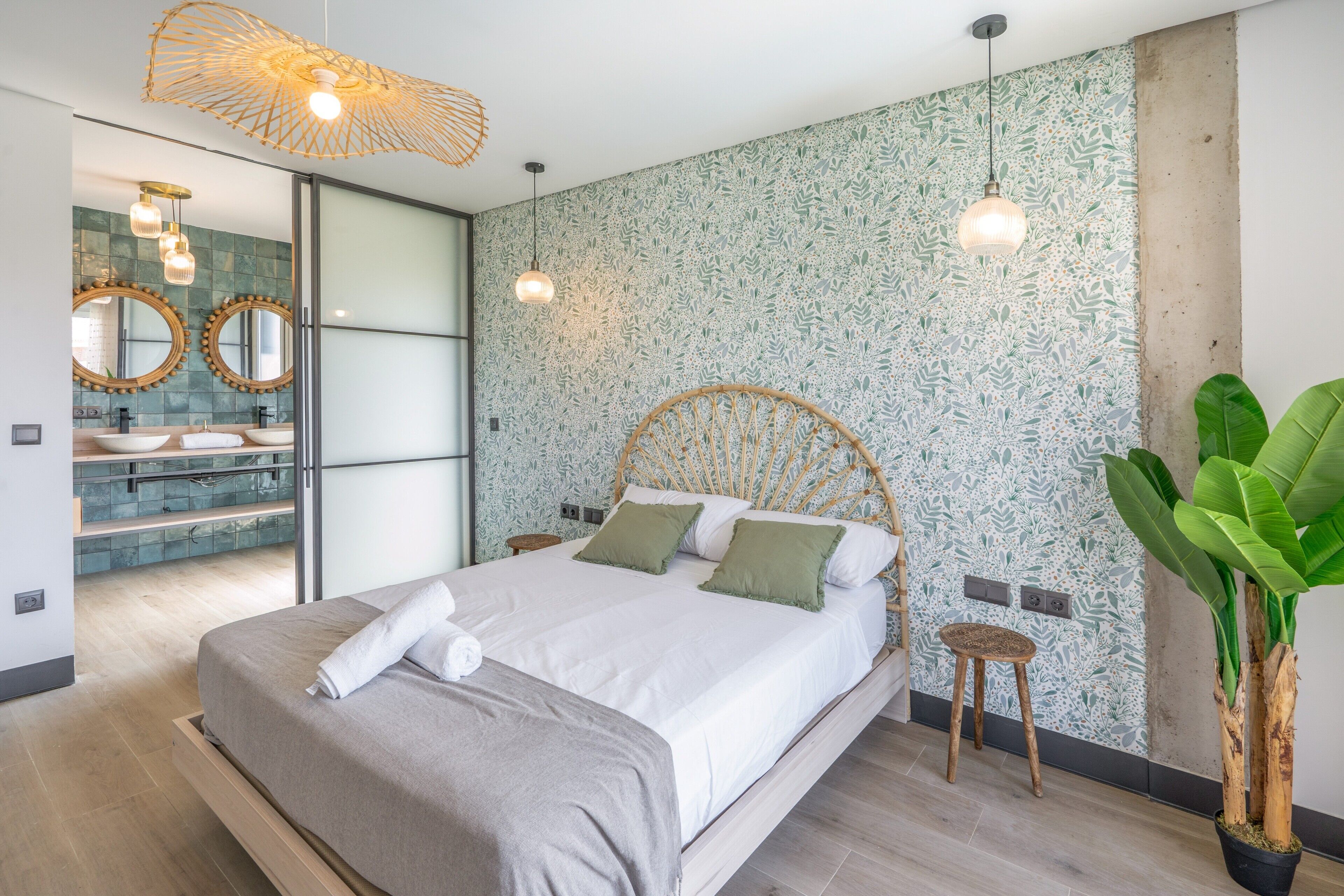 A modern bedroom with a large bed, a bathroom with a round mirror, and a green plant.