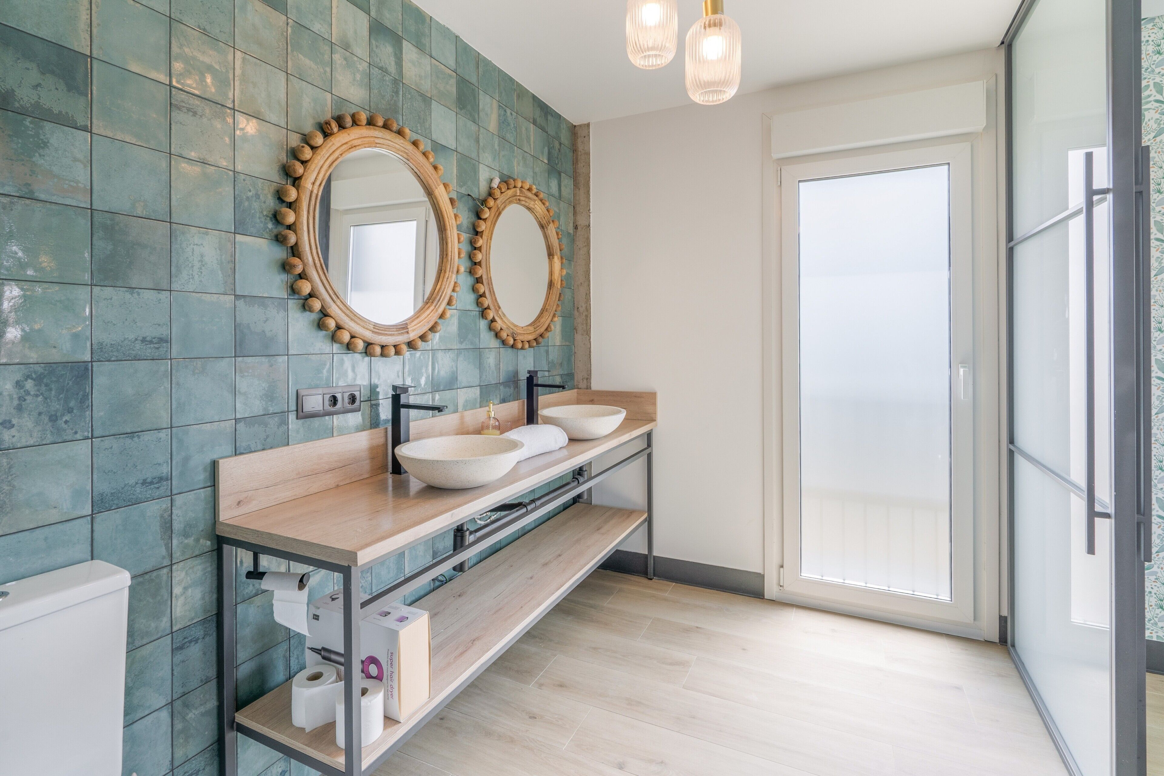 Un baño moderno con dos espejos ovalados, un tocador de madera, un lavamanos y un inodoro.