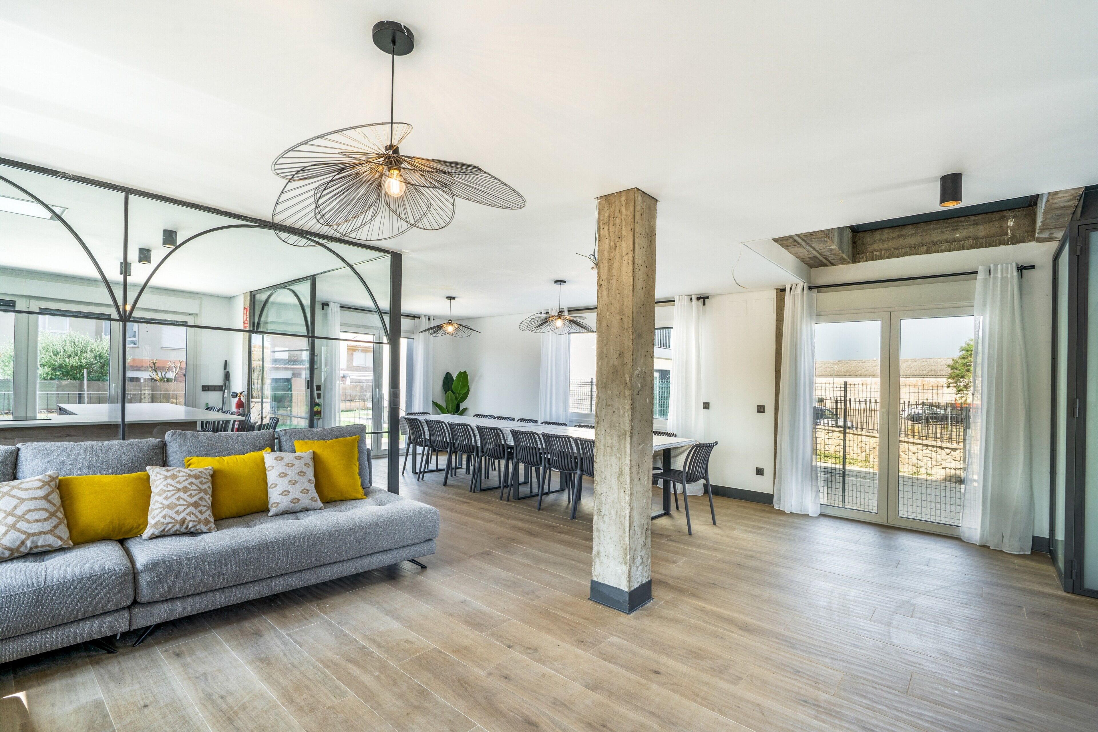 A modern living room with a grey sofa, wooden flooring, and a dining area with a table and chairs.