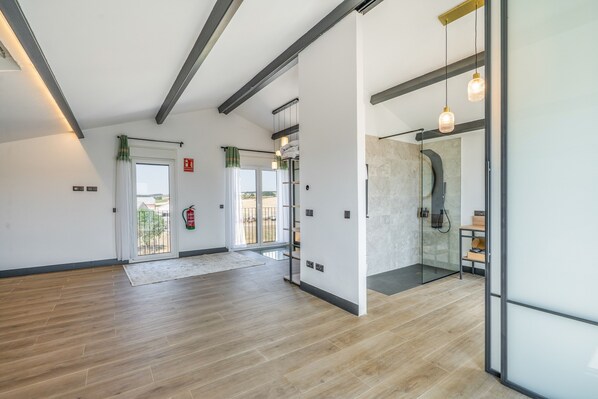 A spacious room with wooden flooring, a glass shower enclosure, and a view through the glass doors.