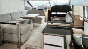 Interior de um iate com área de refeições, assentos e vista para a marina.