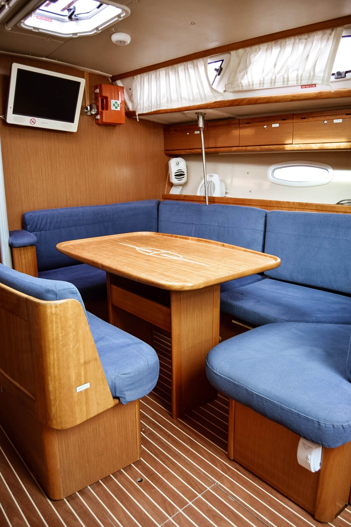 A compact interior with a wooden table, blue cushioned seating, a mounted TV, and a window with curtains.
