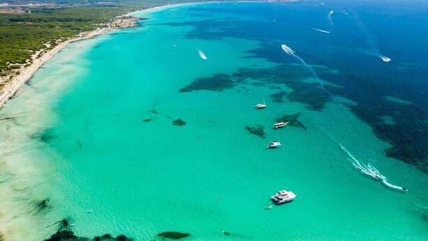 Vista aérea de uma área costeira com águas turquesa cristalinas, barcos e uma praia.