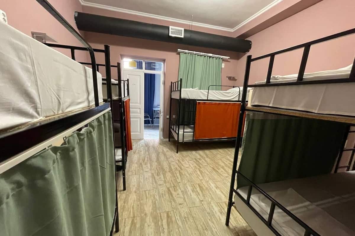 A dormitory room with bunk beds, a door leading to another room, and a window with curtains.