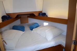 Ein schmaliges Bett mit weißer Bettwäsche und blauen Handtüchern, ein Holz-Kopfteil und eine kleine Holzablage.