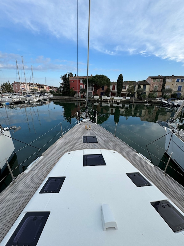 A marina with boats docked, a wooden deck, and buildings in the background.