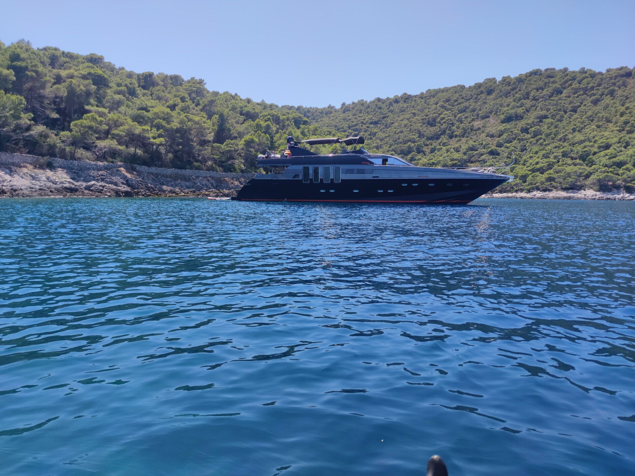 Ein Boot auf ruhigem Wasser, im Hintergrund ein bewaldeter Hügel.