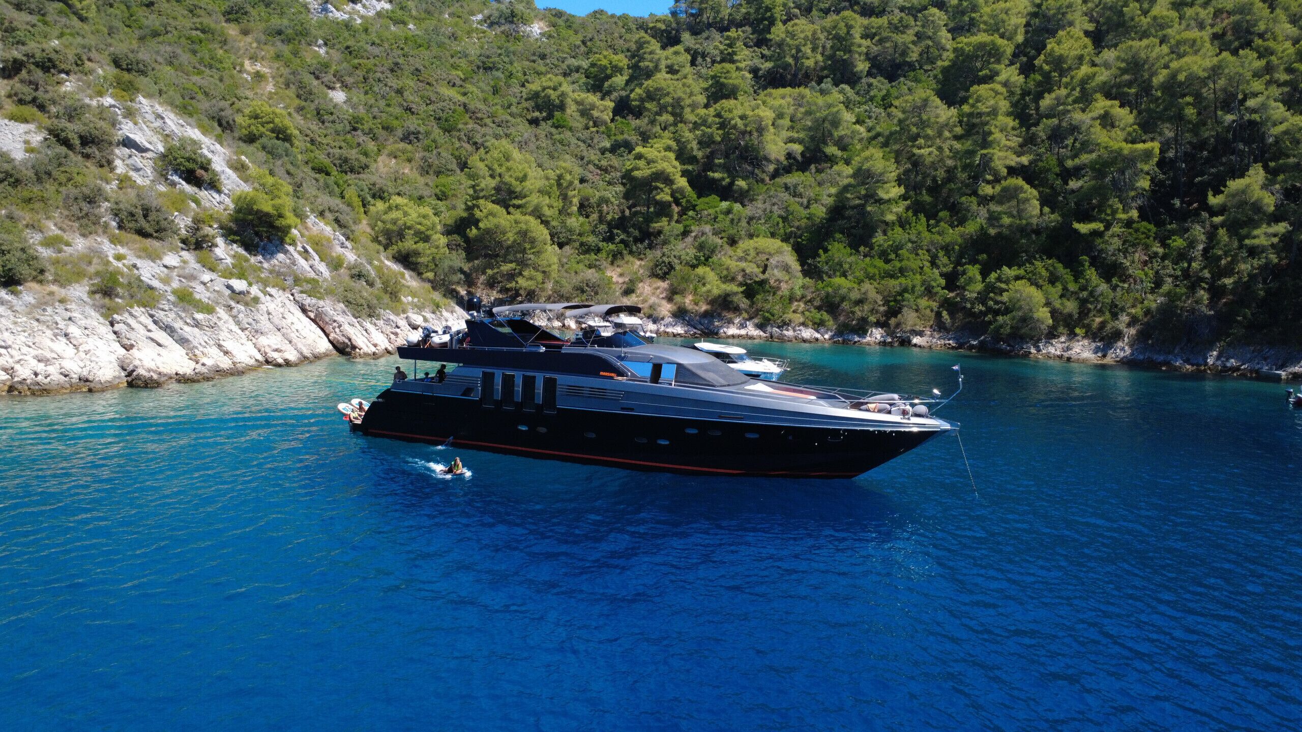A large yacht docked at a marina surrounded by rocky terrain and dense forest.