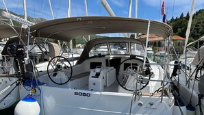 A sailboat named 'BOBO' docked at a marina with other boats, a steering wheel, and a winch visible.