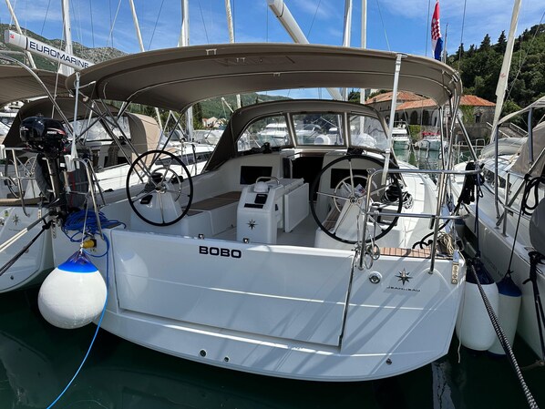 Een zeilboot genaamd 'BOBO' afgemeerd in een jachthaven, met andere boten, een stuurwiel en een lier in het zicht.