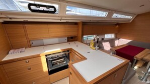 A compact galley with wooden cabinetry, a built-in oven, and a small seating area with a red cushion. - Sun-Kissed Sailing Adventure in Split, Croatia (Kaštel Gomilica)