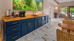 A kitchen with a marble floor, a large painting of a peach orchard, and a dining area with wicker chairs.