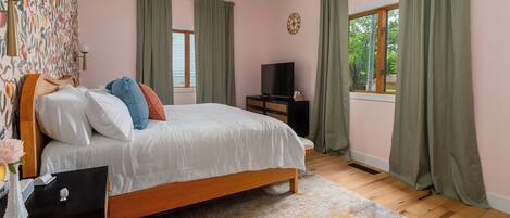 A bedroom with a bed, a TV, a nightstand, a window with curtains, and a patterned wall.