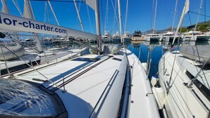 Marina con diverse barche a vela ormeggiate, cielo azzurro limpido e un cartello con scritto 'charter.com'.