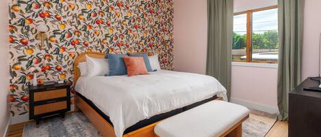 A bedroom with a bed, bedside table, bench, and a window with curtains.