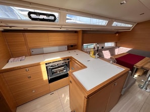 A compact galley with wooden cabinetry, a built-in oven, and a small seating area with a red cushion.