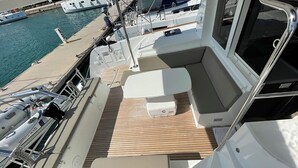 A boat deck with seating, a small cooler, and a window. - Sun-kissed Sailing Adventure in Split-Dalmatia, Croatia (Seget Donji)
