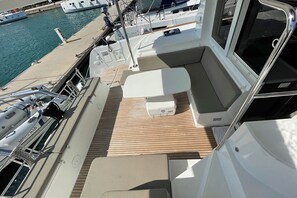 Ein Bootsdeck mit Sitzgelegenheiten, einer kleinen Kühlbox und einem Fenster.