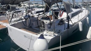 Een zeilboot afgemeerd in een jachthaven met een overdekte kuip, stuurwiel en diverse touwen en uitrusting.