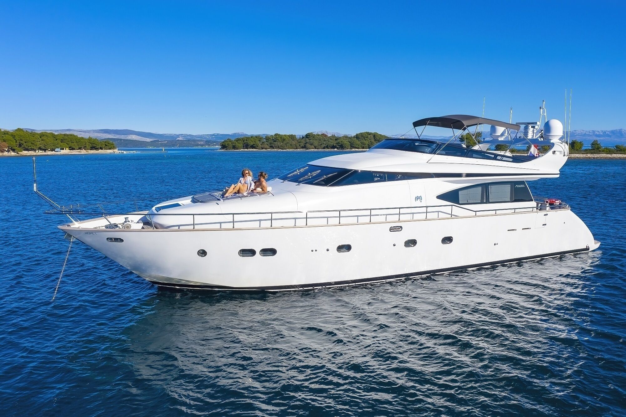 En stor, vit yacht med ett övre däck som är delvis täckt, flera fönster och en synlig mast.