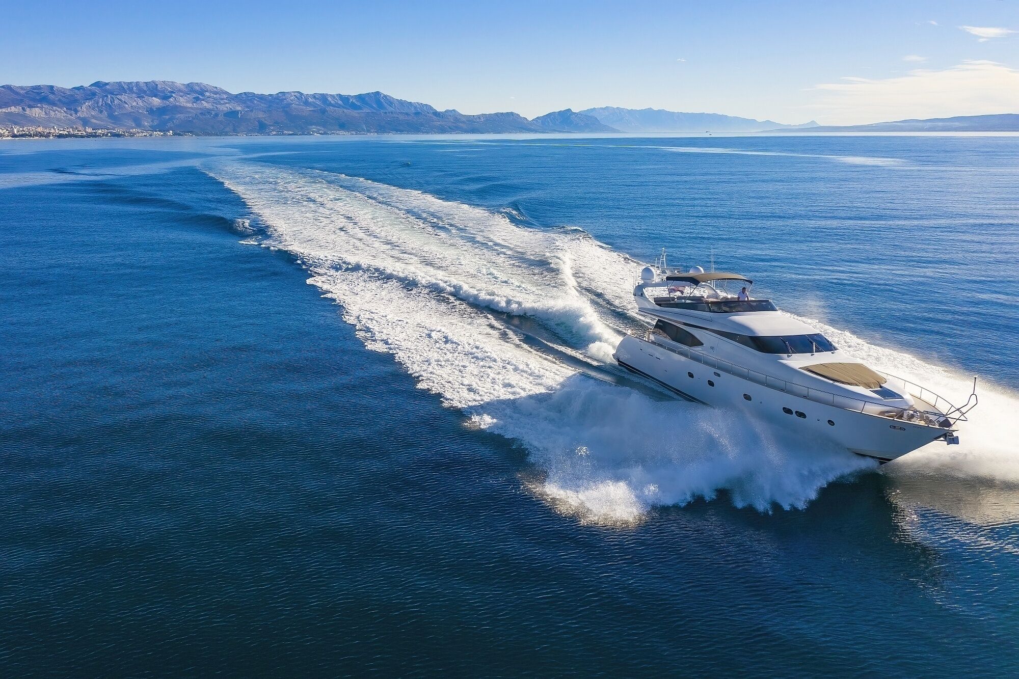 A yacht cruising on a calm sea with a mountainous coastline in the background.