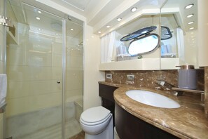 A bathroom with a glass shower enclosure, a white toilet, a marble sink, and a mirror with a towel rack.
