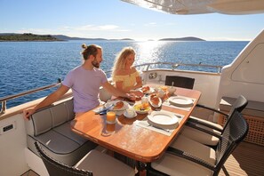 A couple dining on a boat with a table set for breakfast, surrounded by water and distant land.