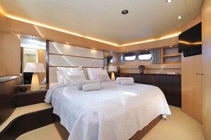 A spacious bedroom with a large bed, bedside tables, a TV, and a window with curtains.
