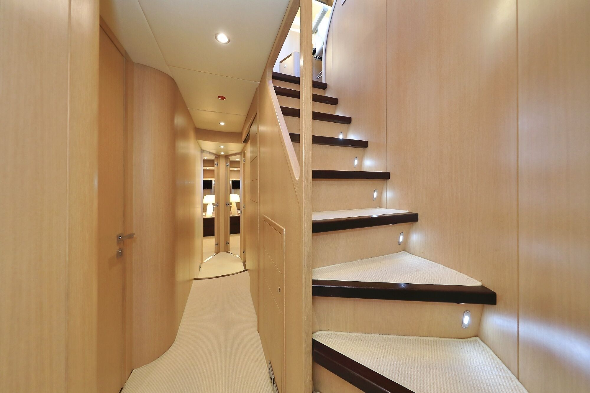 A narrow hallway with a wooden staircase and a mirrored wall.