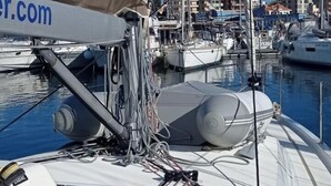 Ein Yachthafen mit mehreren Segelbooten an den Liegen, ein überdachter Bereich mit einem Logo und eine Stadtlandschaft im Hintergrund.