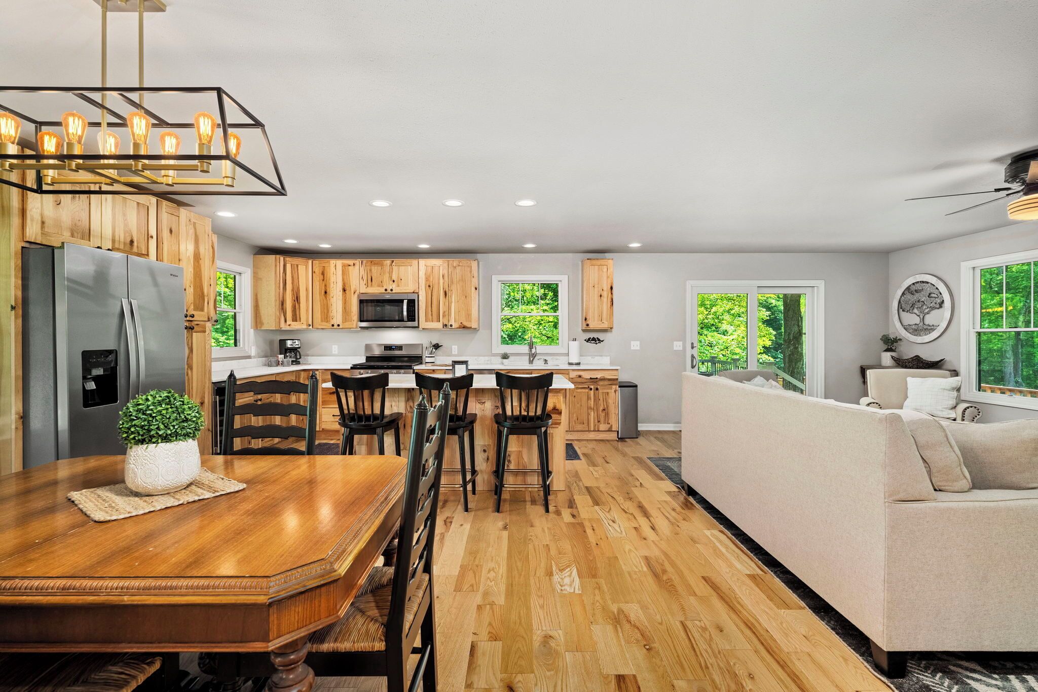 Una cocina moderna con armarios de madera, un comedor con mesa y sillas de madera, y una sala de estar con sofá y ventanas amplias.