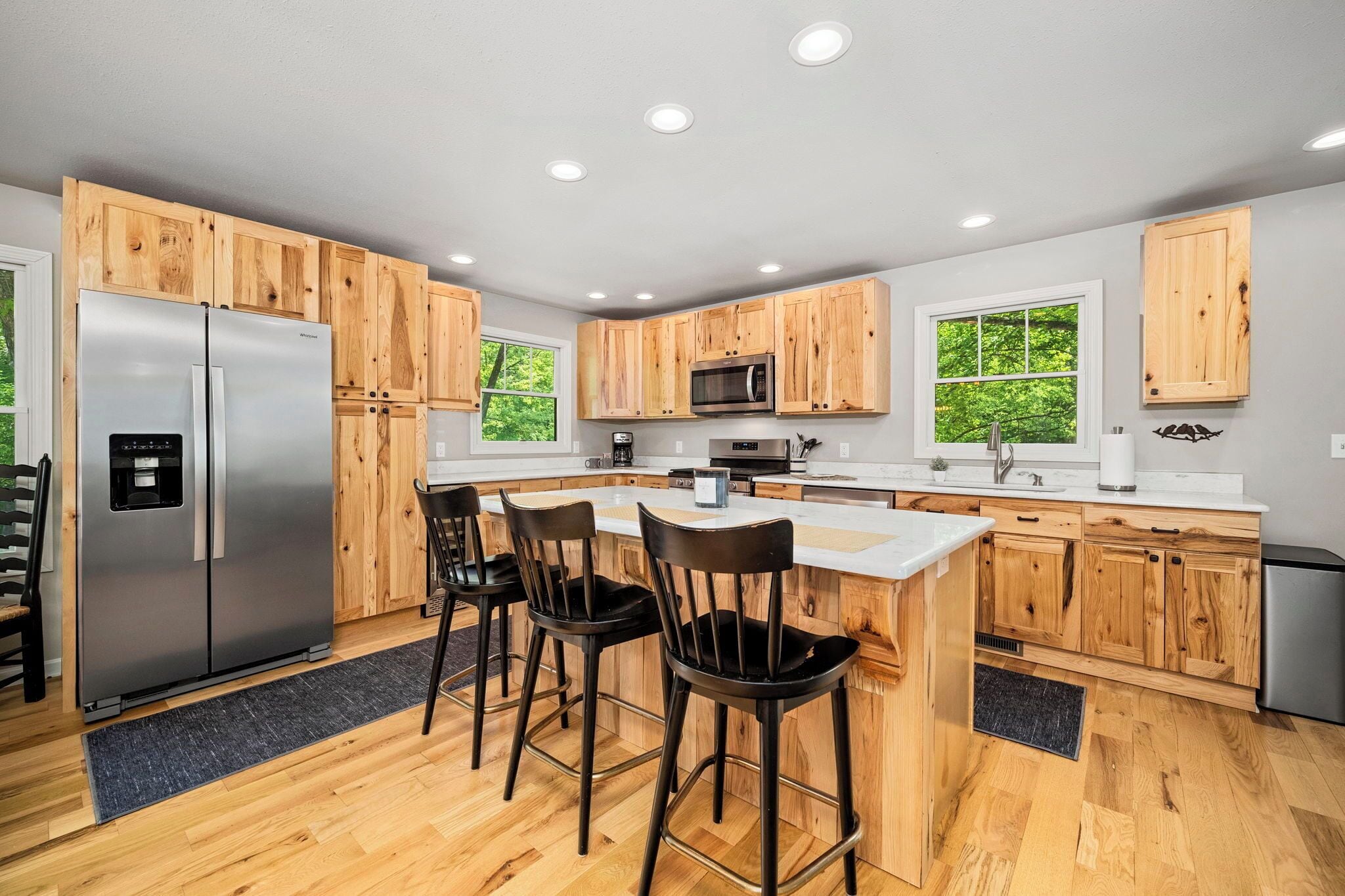 Une cuisine moderne avec des meubles en bois, des appareils électroménagers en acier inoxydable, un coin bar et de grandes fenêtres.