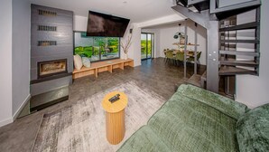 Ein modernes Wohnzimmer mit einem grünen Sofa, einem Holztisch, einem Kamin und einem Essbereich mit Blick.