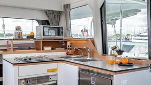 Een compacte keuken met een magnetron, spoelbak en kookplaat, met uitzicht op de jachthaven door grote ramen.