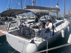 Eine Segelyacht liegt in einer Marina vor Anker, mit einem überdachten Cockpit, Steuerpult und verschiedenen Leinen und Ausrüstungsgegenständen.