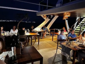 An outdoor dining area with tables and chairs, a view of the city at night, and a staircase leading to an upper level. - Getway with an incredible pool Marina Bay view! (Cabo San Lucas)