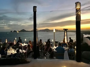 Een terras met tafels en stoelen, met uitzicht op een waterpartij en verre landschappen.