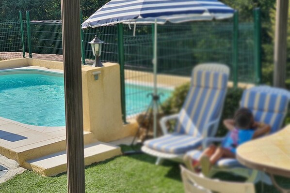 A swimming pool with lounge chairs and a table, surrounded by a green fence. - Ground Floor of a Villa for Rent for a Dream Vacation in a Peaceful Natural Setting (Les Adrets-de-l'Estérel)